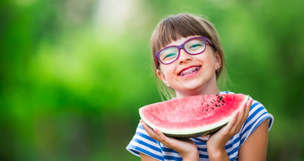 Girl with braces holds a watermelon and smiles.
