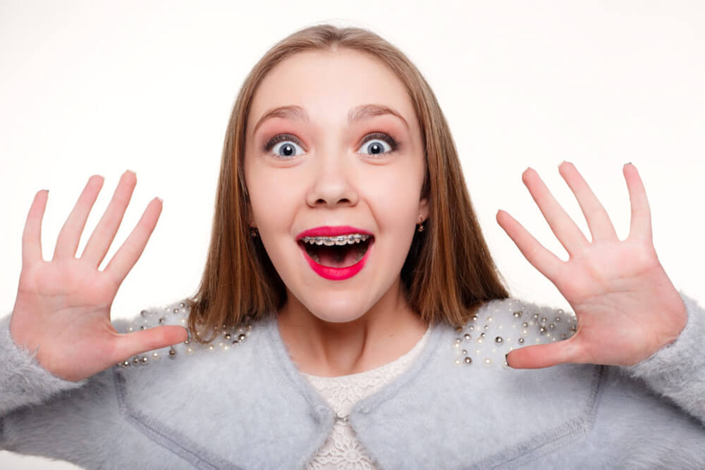 Surprised girl wearing braces holds up hands.
