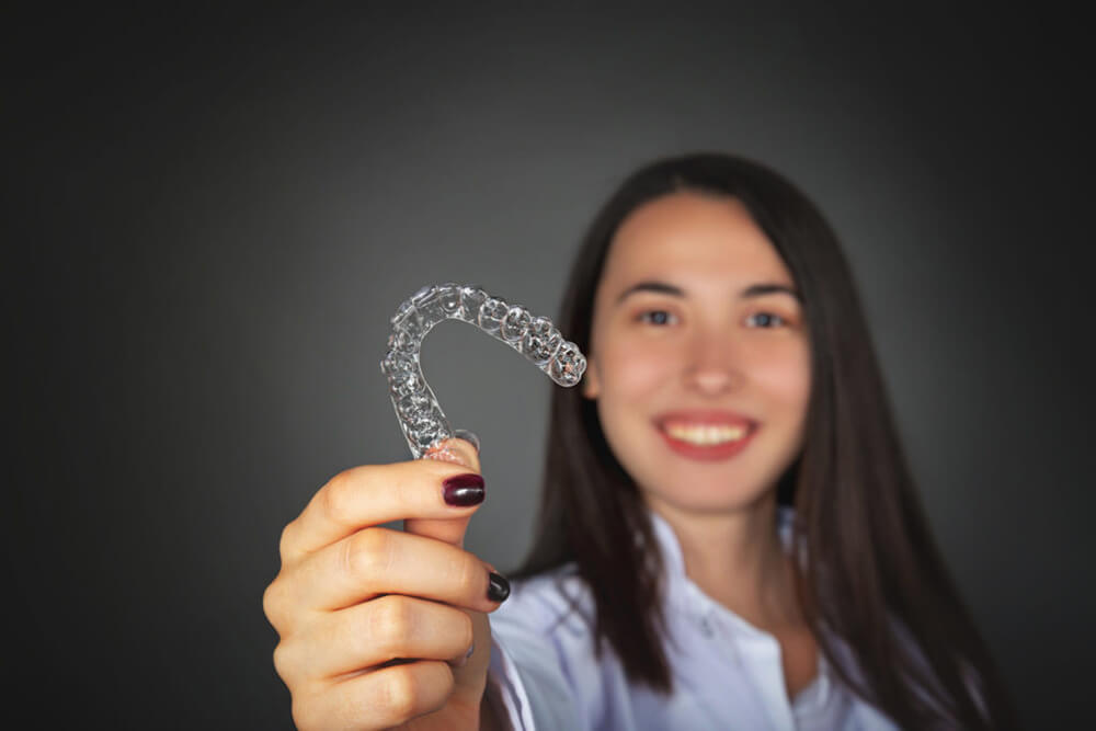 A smiling teenage girl holds an Invisalign treatment.