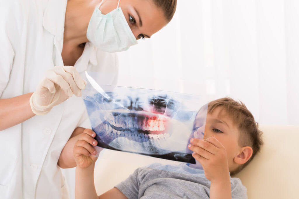 A dentist explains what is occurring with a child’s teeth according to an X-Ray.ing to an X-Ray.