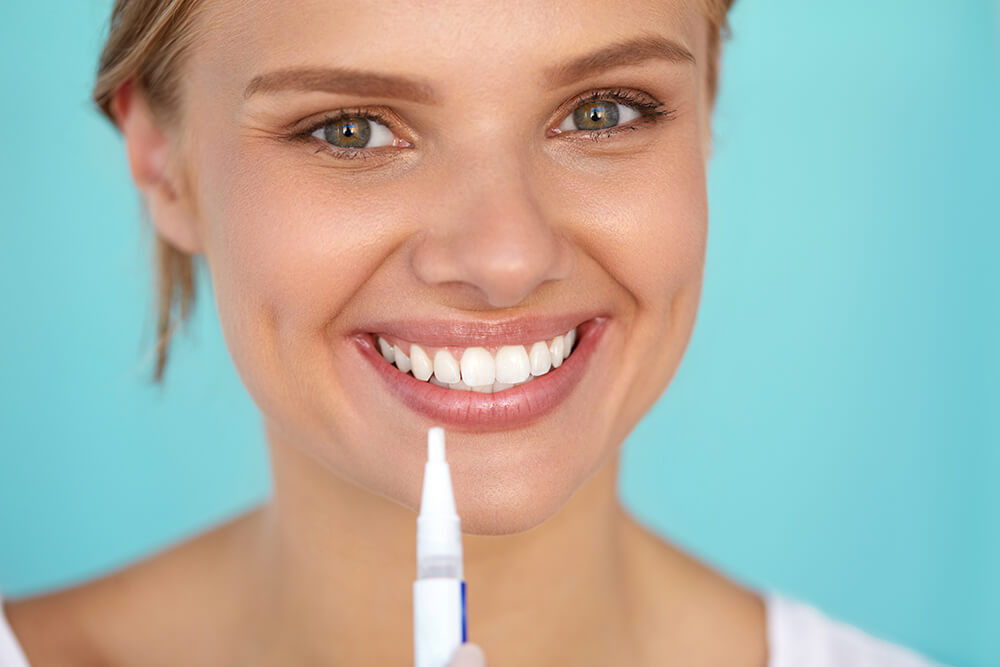 Woman smiling and holding teeth whitening pen