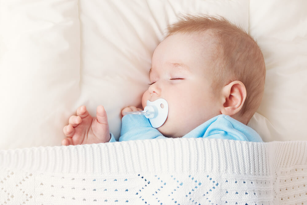 A baby sleeps with a pacifier in his mouth.
