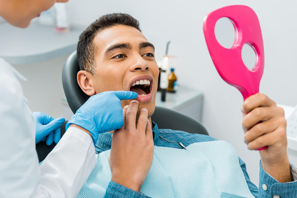 Man looking in the mirror as a dentist shows him something about his teeth