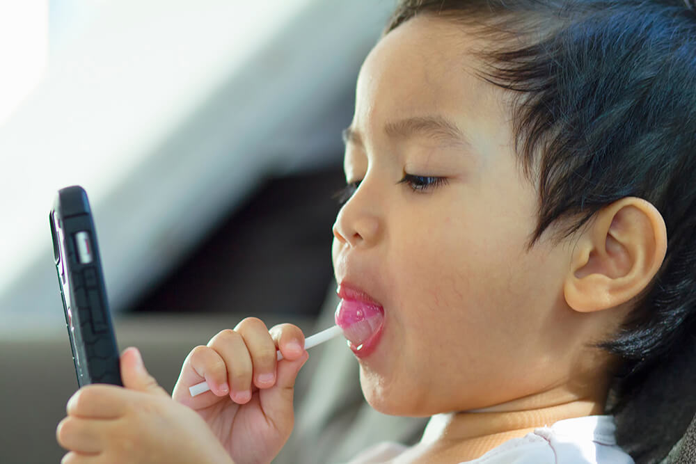 Small kid eating a pink lollipop