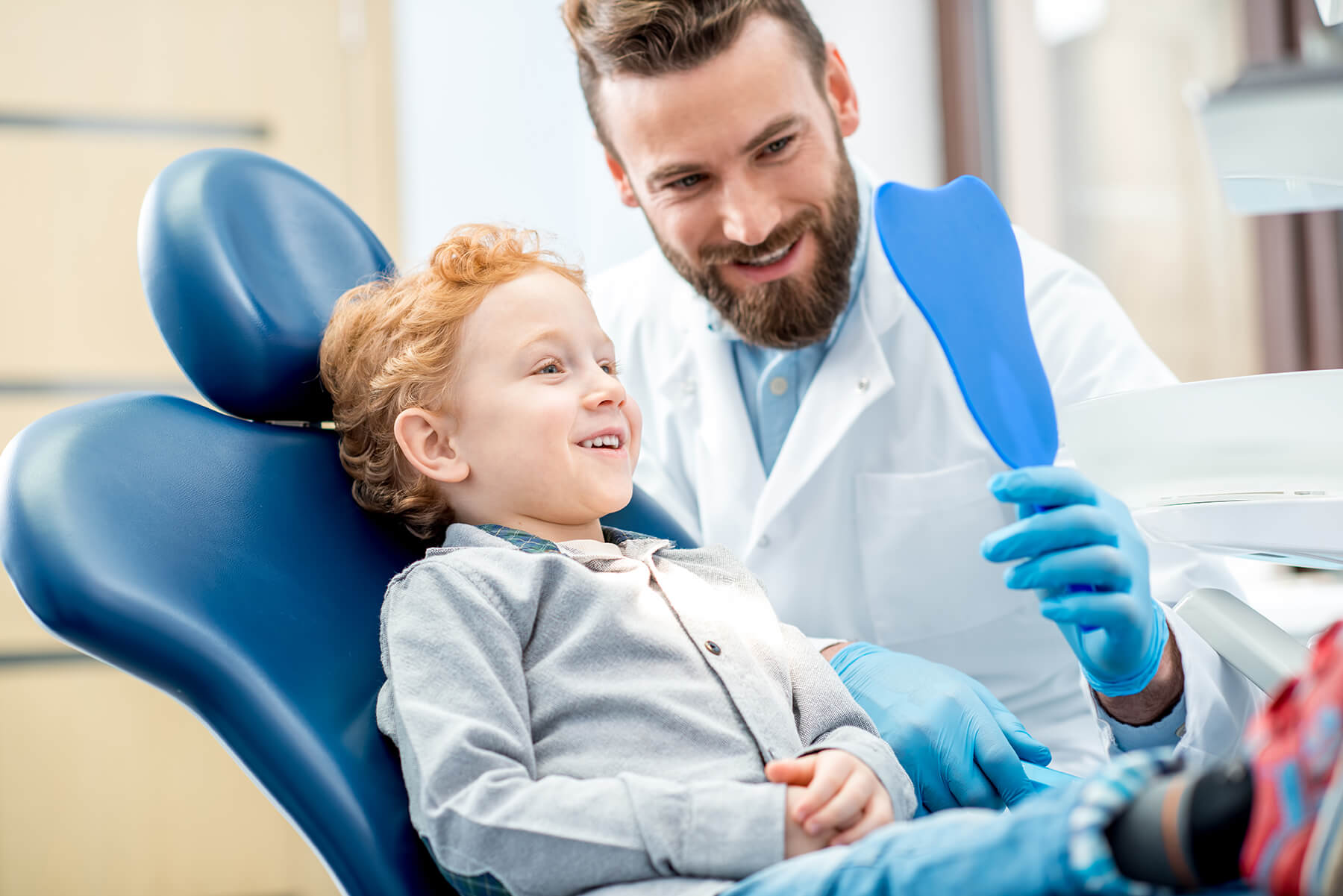 Young boy sits in dental chair and looks in dental mirror