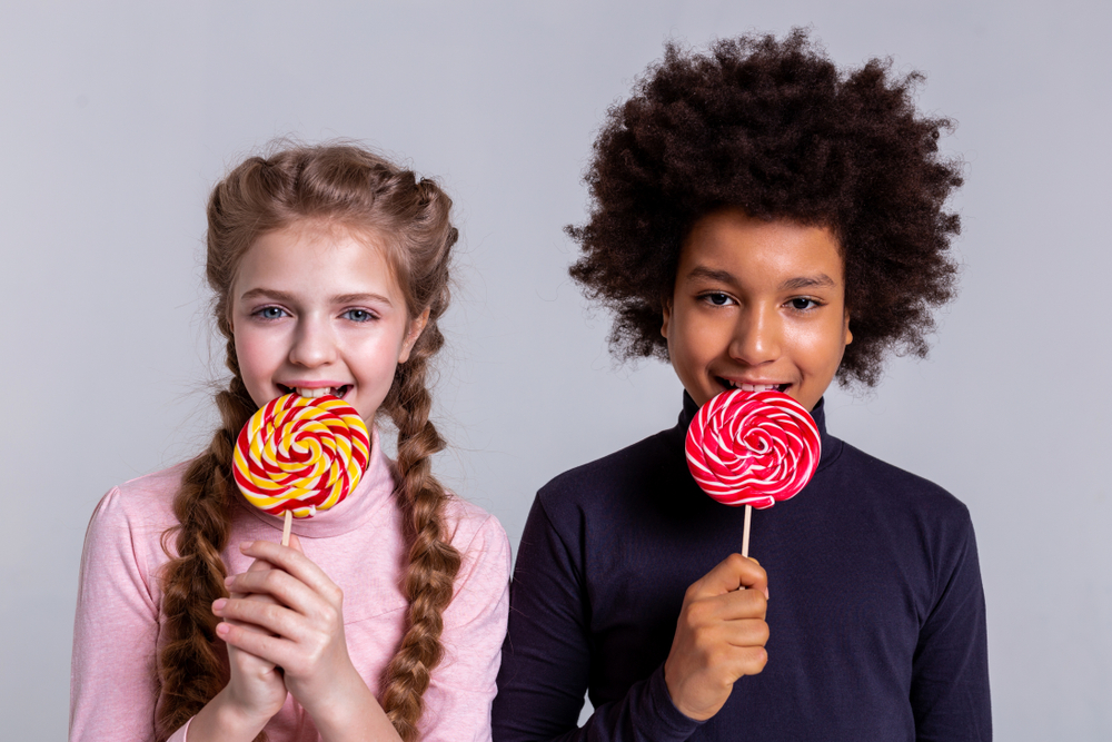 Two kids eating large lollipops