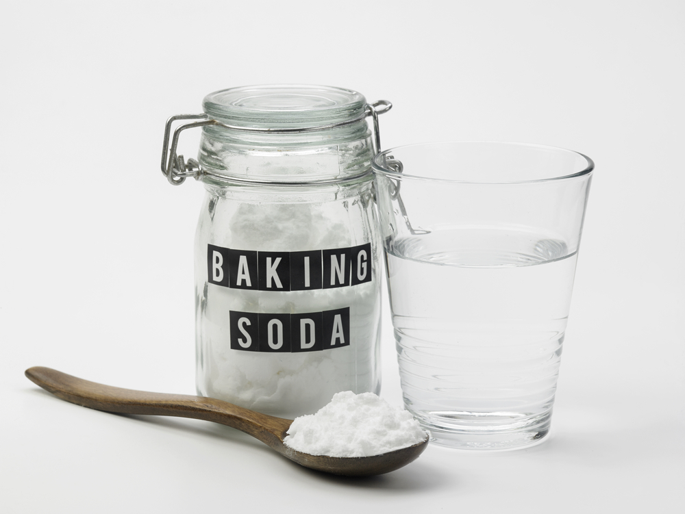 baking soda in glass container with glass of water and wooden spoon