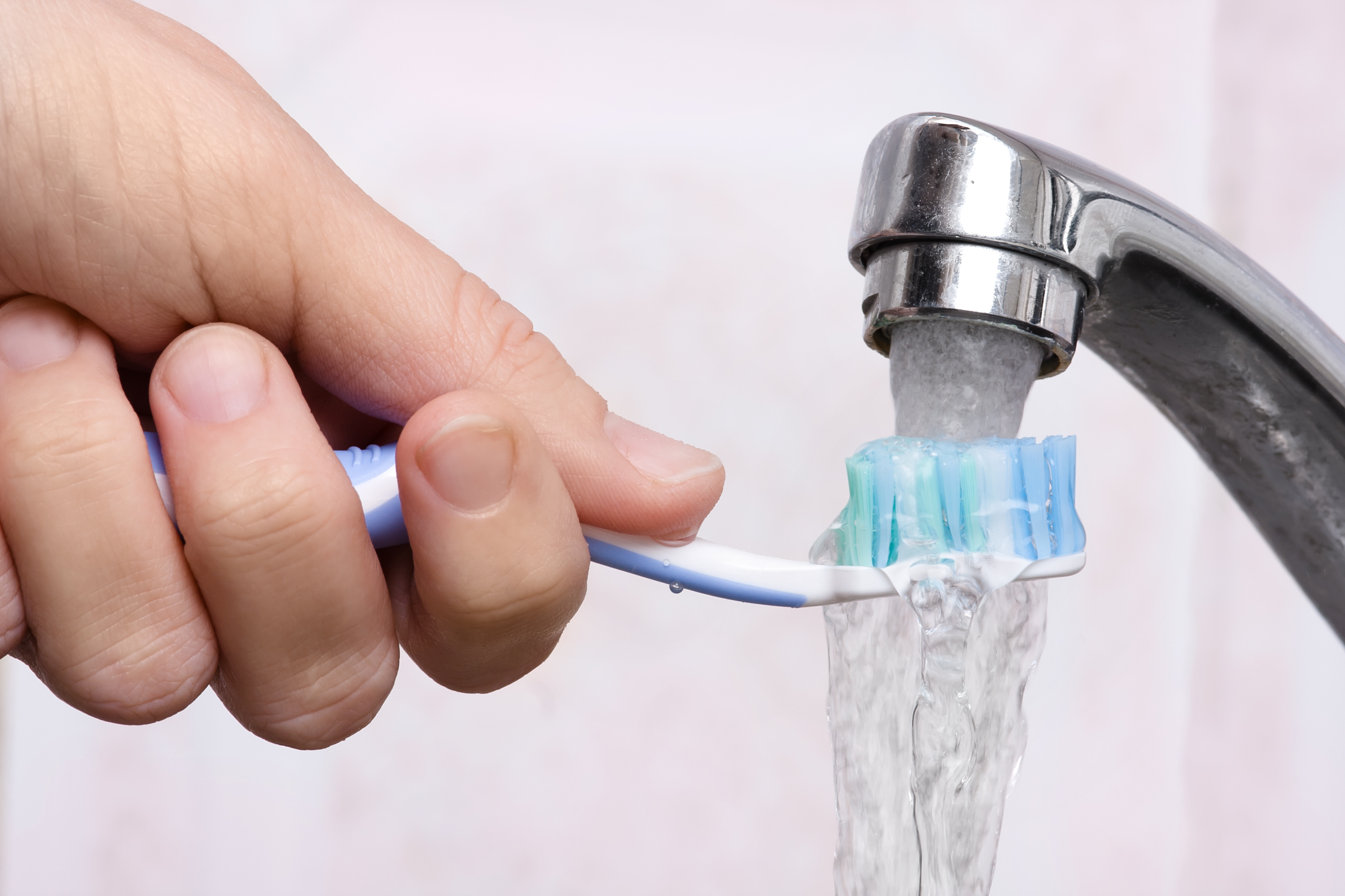Man's Hand Holding a Toothbrush Under Running Water