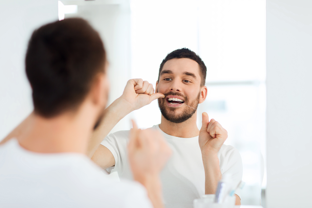 Man Looking in Mirror Flossing His Teeth