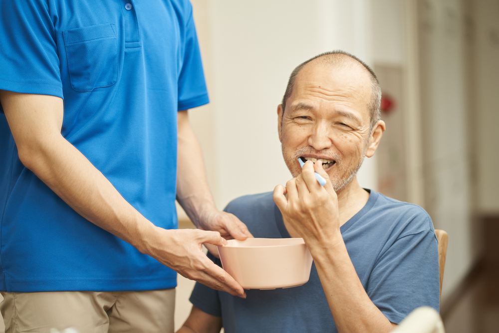 Man caring for an elderly relative by brushing teeth