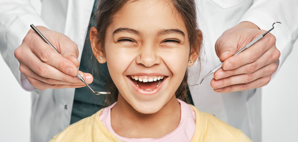 Smiling girl with dentist holding dental tools