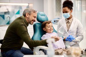 Happy father holding a mirror while son is looking at his teeth after a dental appointment at a trusted dentist’s office.
