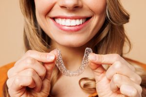 Smiling woman holding a clear Invisalign aligner tray before orthodontic treatment